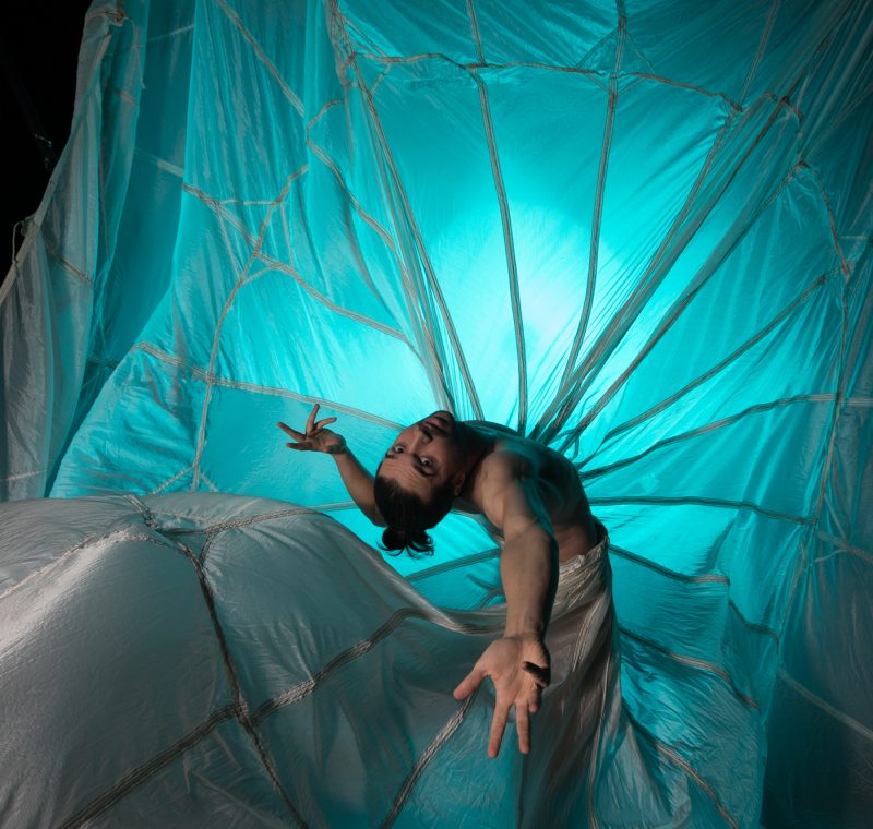A dancer arches backward while surrounded by a large piece of flowing, translucent fabric