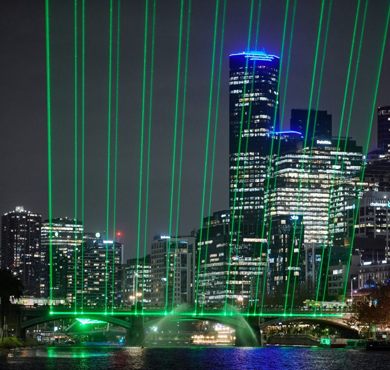 A cityscape at night time with green lasers shining upwards